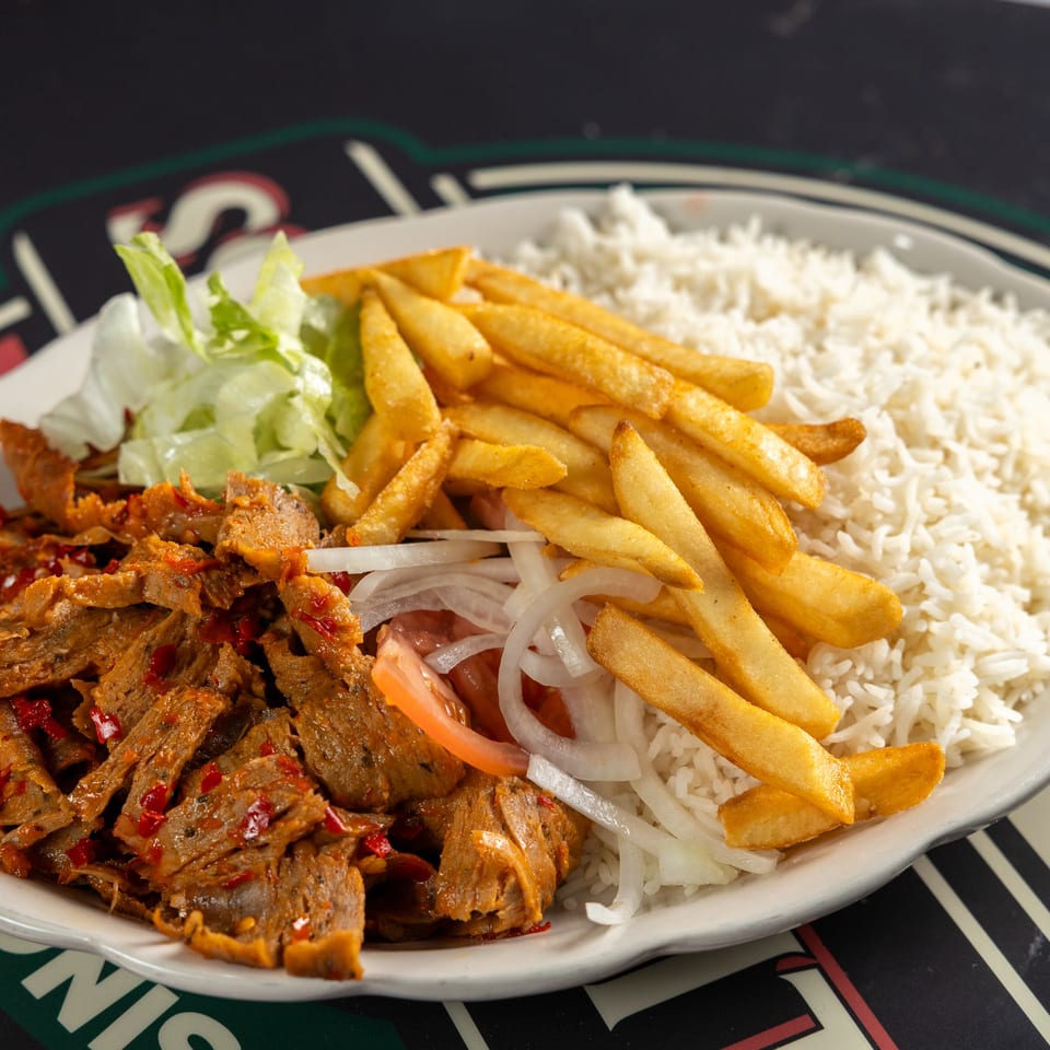 Plate of seasoned sliced meat, French fries, white rice, lettuce, tomatoes, and onions.